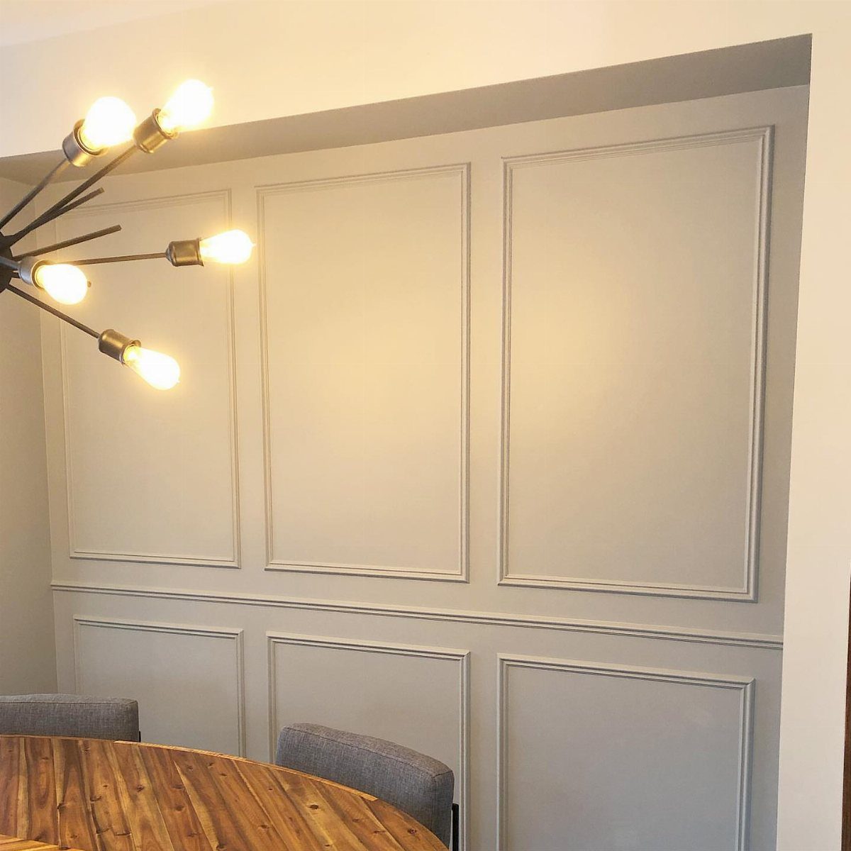 Paneled grey wall with decorative molding and a chair rail above a wooden dining table.