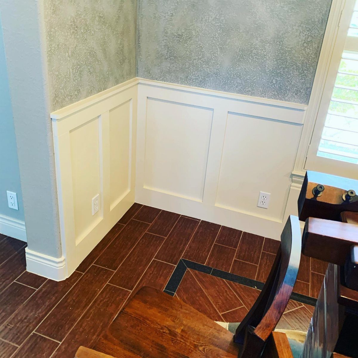 White wainscoting with rectangular panel molding installed on a wall with blue textured wallpaper.