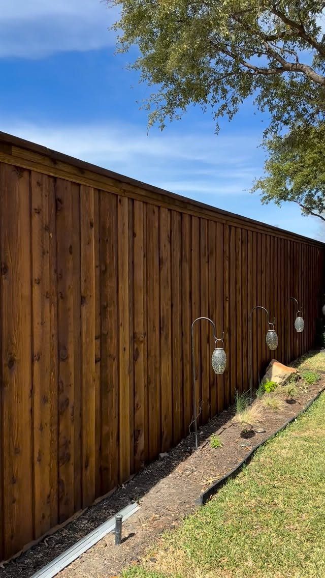 A tall vertical wooden privacy fence with a dark brown stain next to a garden bed.
