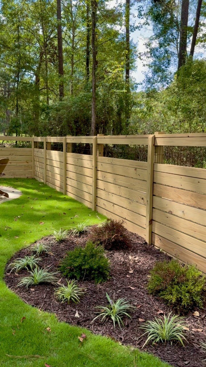 Horizontal wooden planks form a fence bordering a green lawn and a small garden bed.
