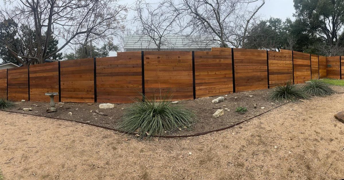 A modern horizontal wooden fence with black metal posts bordering a landscaped garden bed.
