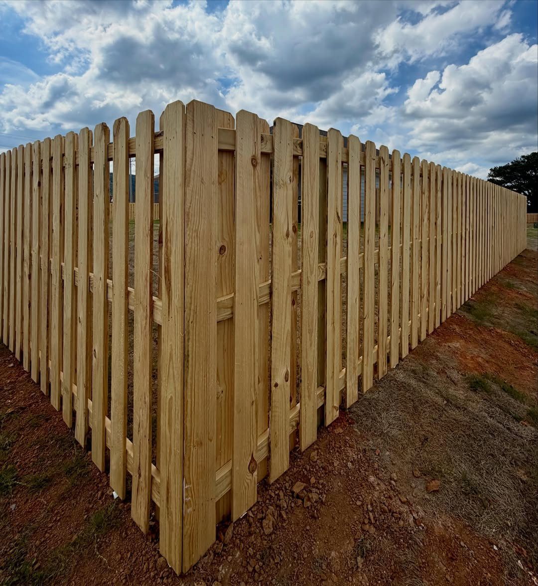 A new wooden shadowbox fence installed around a corner of a dirt yard under a cloudy sky.