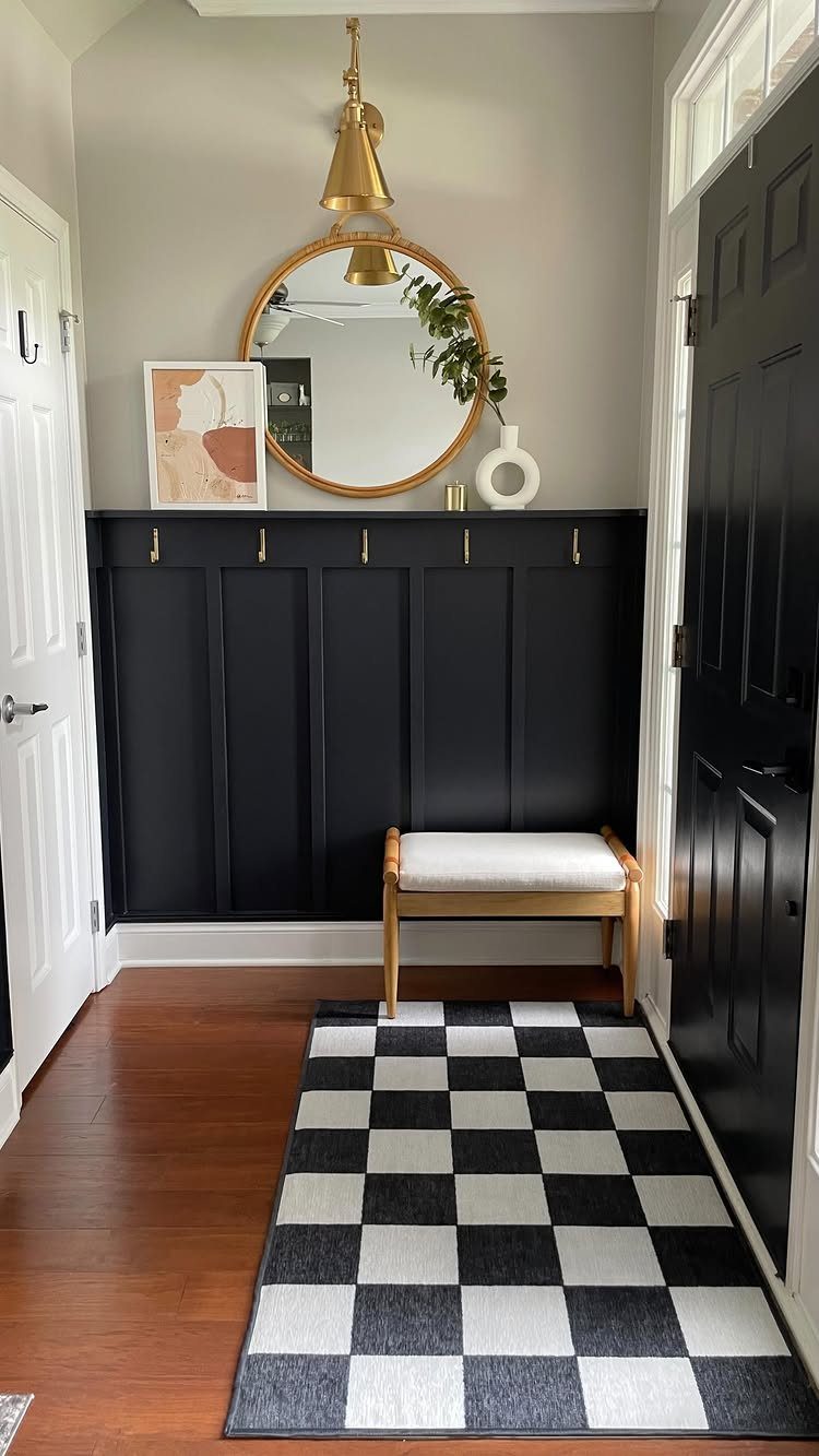 Black board and batten wainscoting with gold hooks in a modern entryway with a checkered rug.