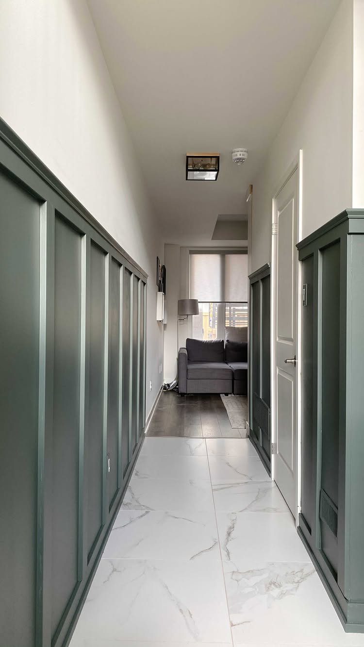 Dark green board and batten wainscoting installed along a hallway with white marble flooring.