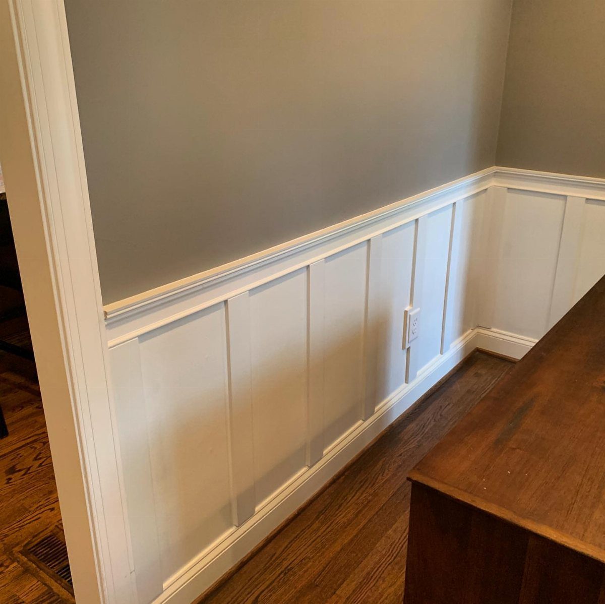 White board and batten wainscoting installed on a grey wall above a wooden floor.