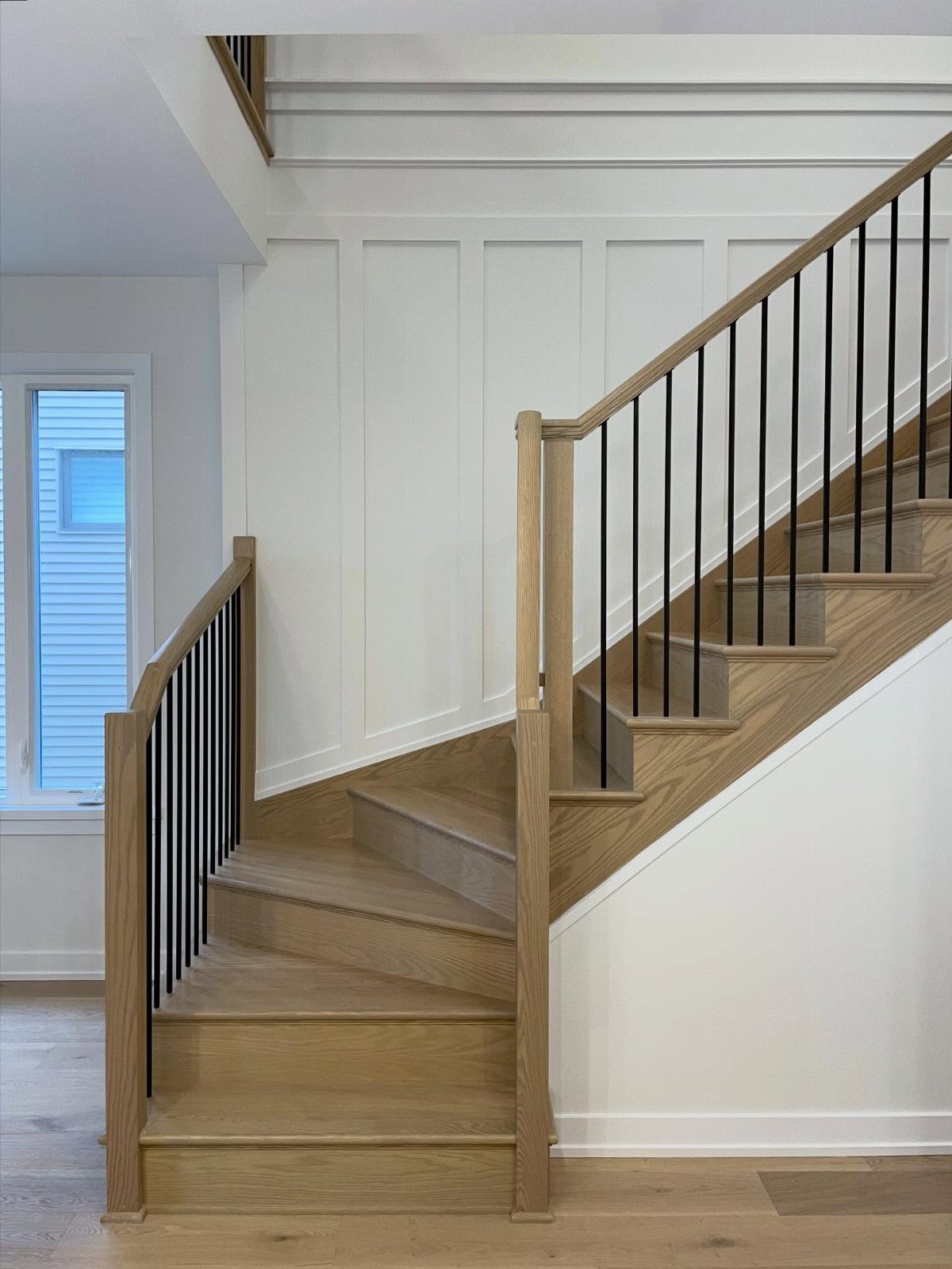 Wooden staircase with black spindles and white board and batten wall paneling in a bright room.