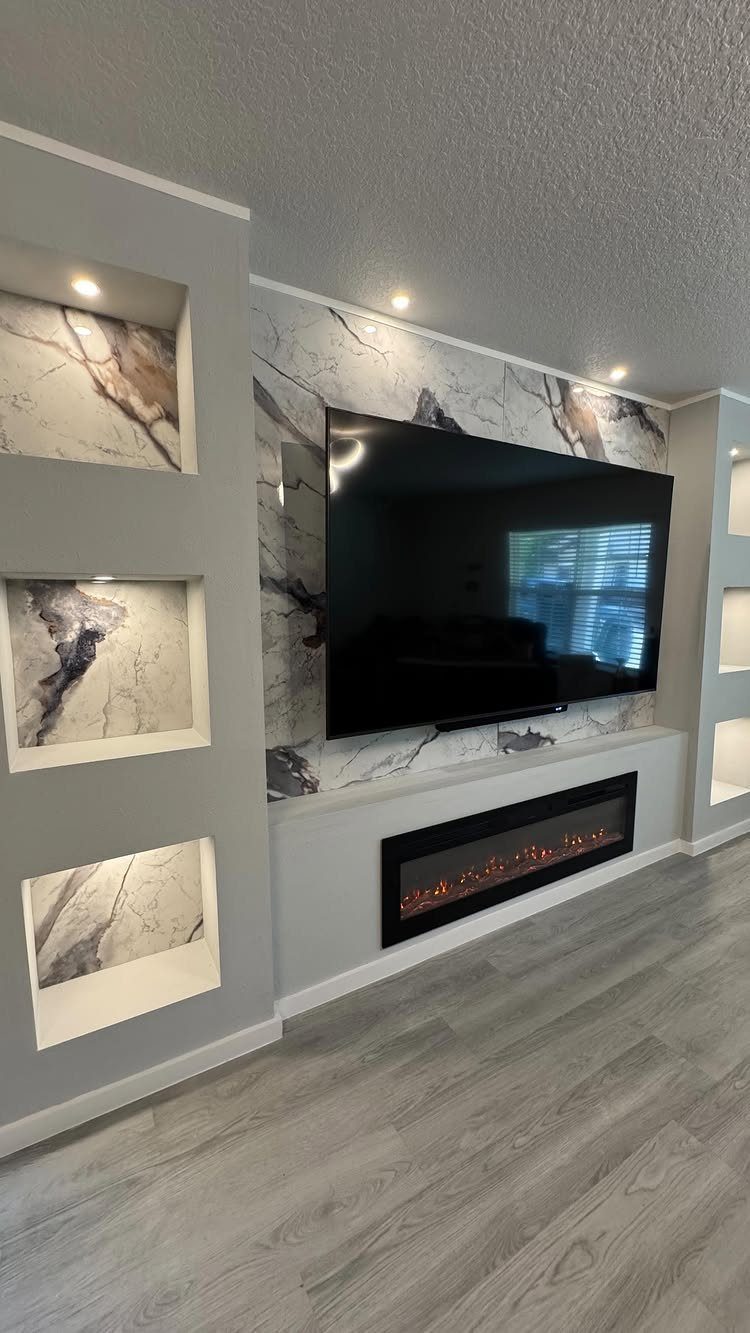 Built in Entertainment Center: 8 Design Ideas for Your Wall 6 A modern entertainment center with a marble-patterned wall, a large television, and a built-in electric fireplace.