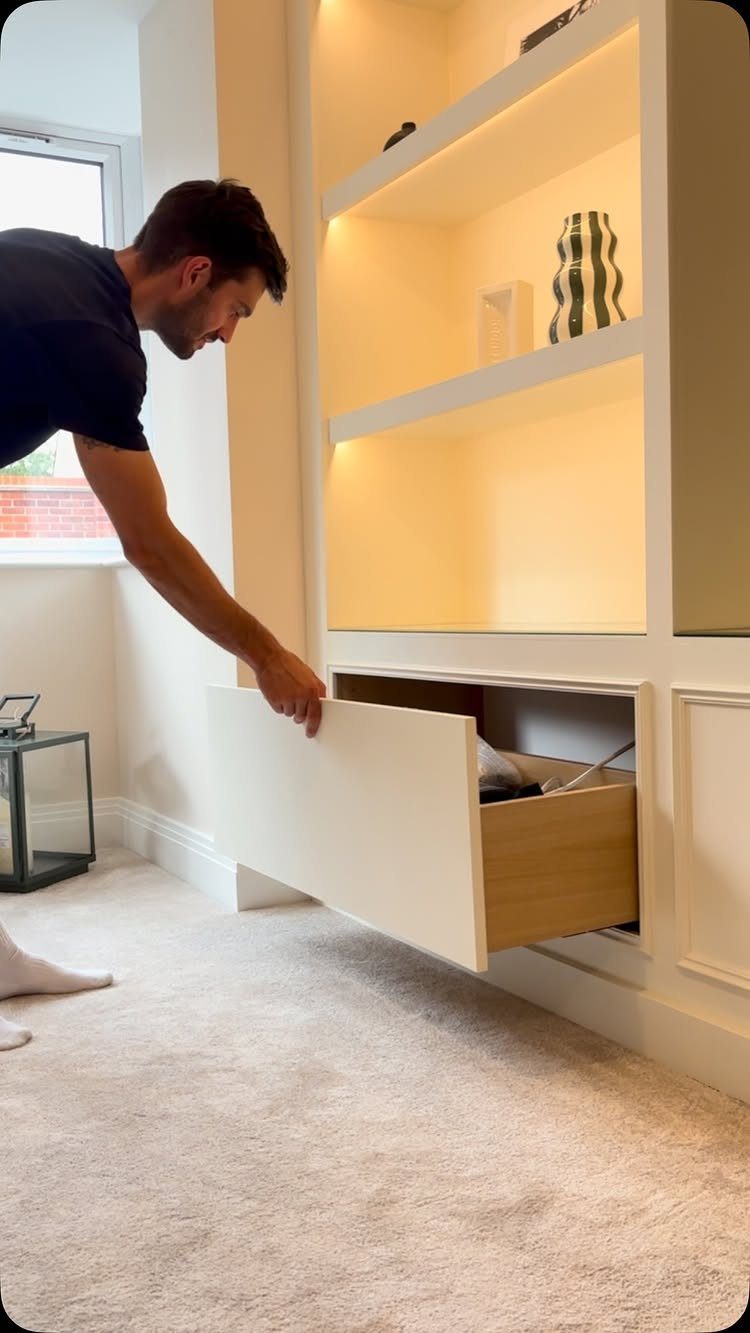 Built in Entertainment Center: 8 Design Ideas for Your Wall 2 A man opening a large white built-in drawer at the base of illuminated shelving units.