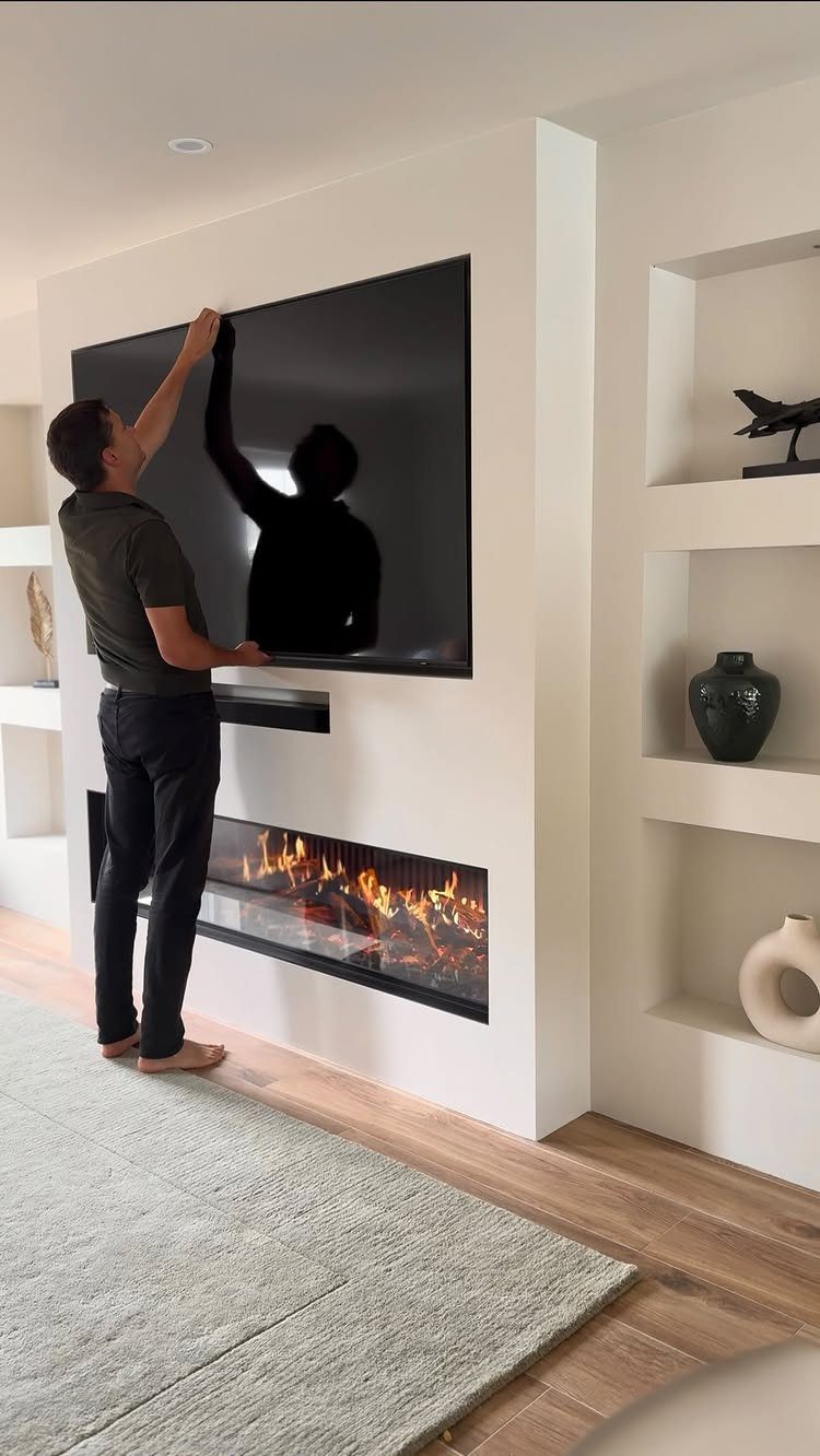 Built in Entertainment Center: 8 Design Ideas for Your Wall 4 A man mounting a large television on a white wall above a modern fireplace.