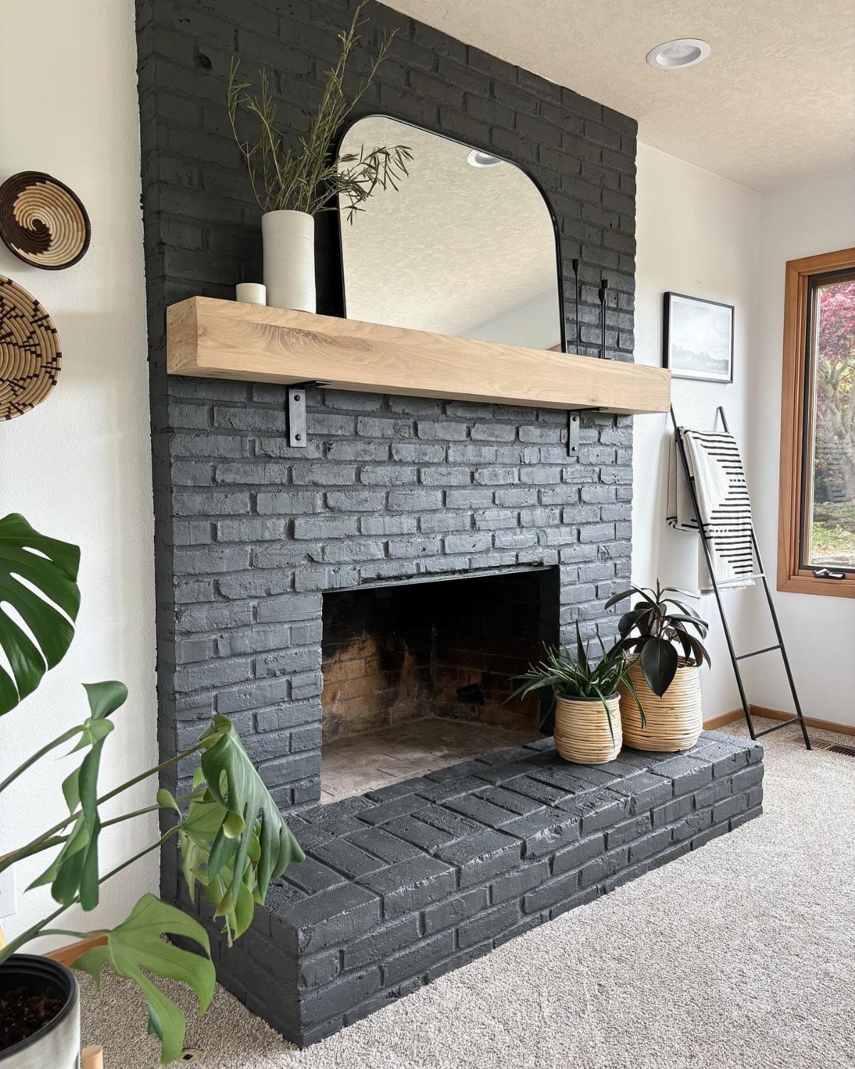 20 Dark Accent Wall Ideas to Try in Any Room 9 A black painted brick fireplace with a light wood mantel and an arched mirror above it.