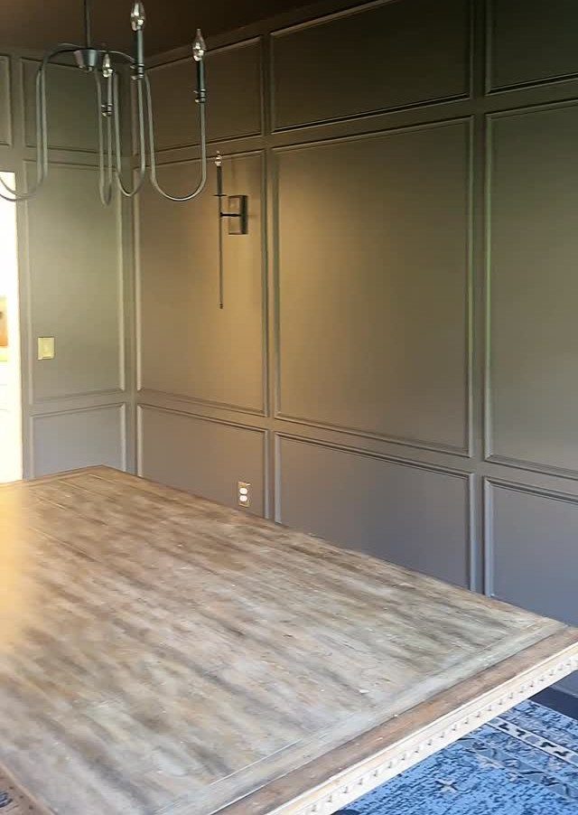 20 Dark Accent Wall Ideas to Try in Any Room 19 Dark paneled walls in a dining room with a large wooden table and black chandelier.