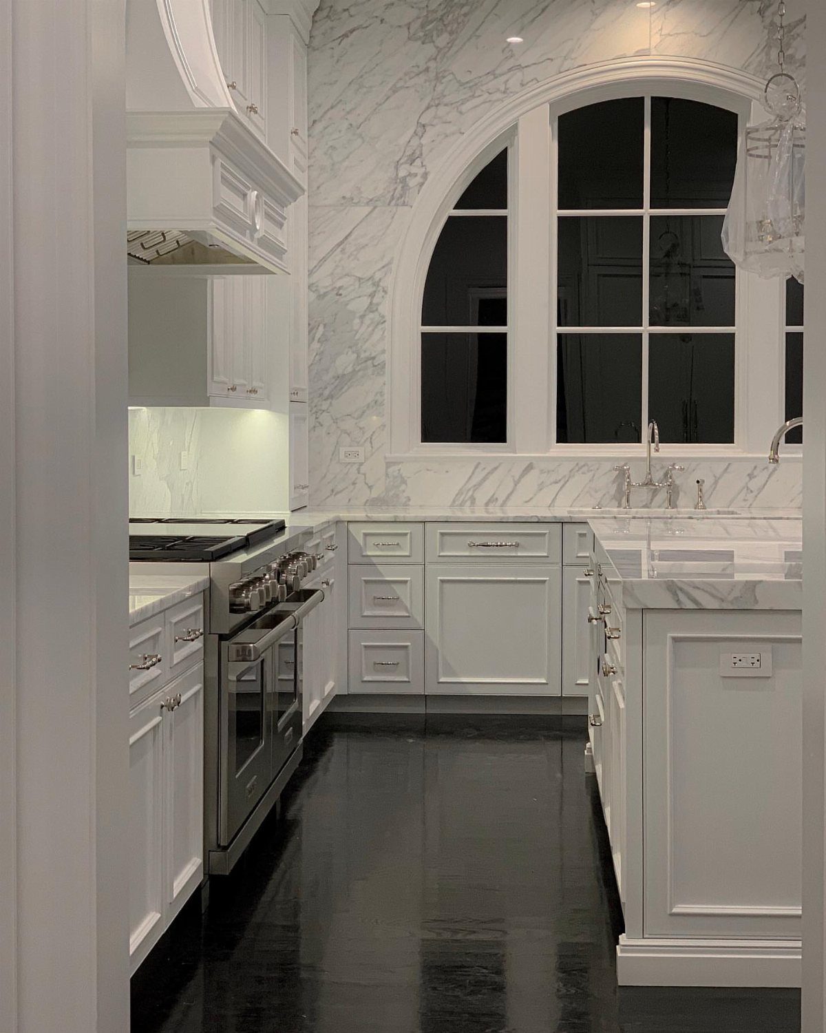 Polished black hardwood floors reflecting white kitchen cabinets and marble countertops in a luxury home.