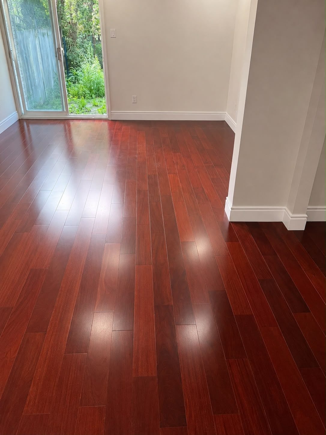 Glossy dark cherry hardwood flooring with reddish-brown planks in an empty room with white walls.