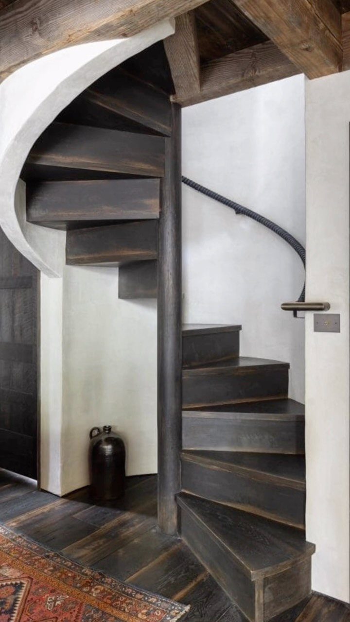 Dark wooden spiral staircase next to white walls and dark hardwood flooring.