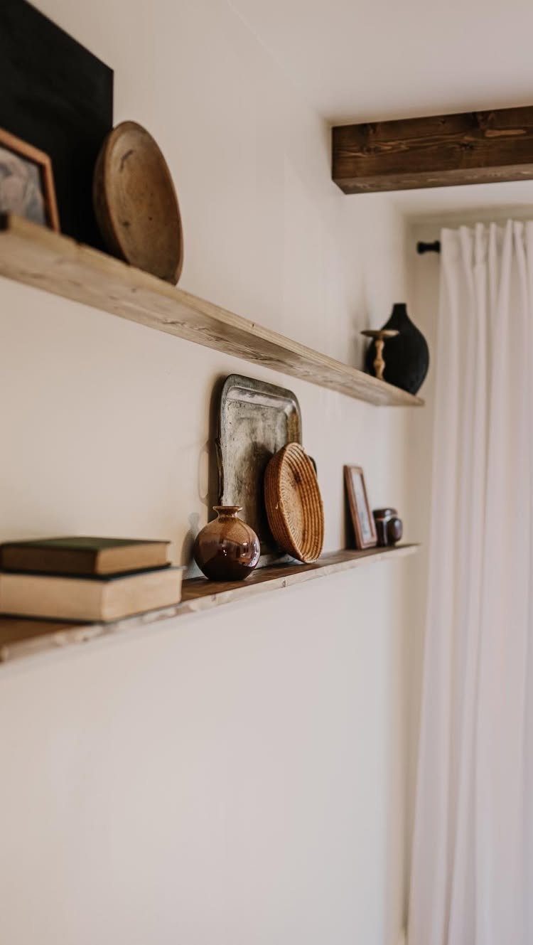 Two rustic wooden floating shelves on a white wall holding books, vases, and decorative bowls.
