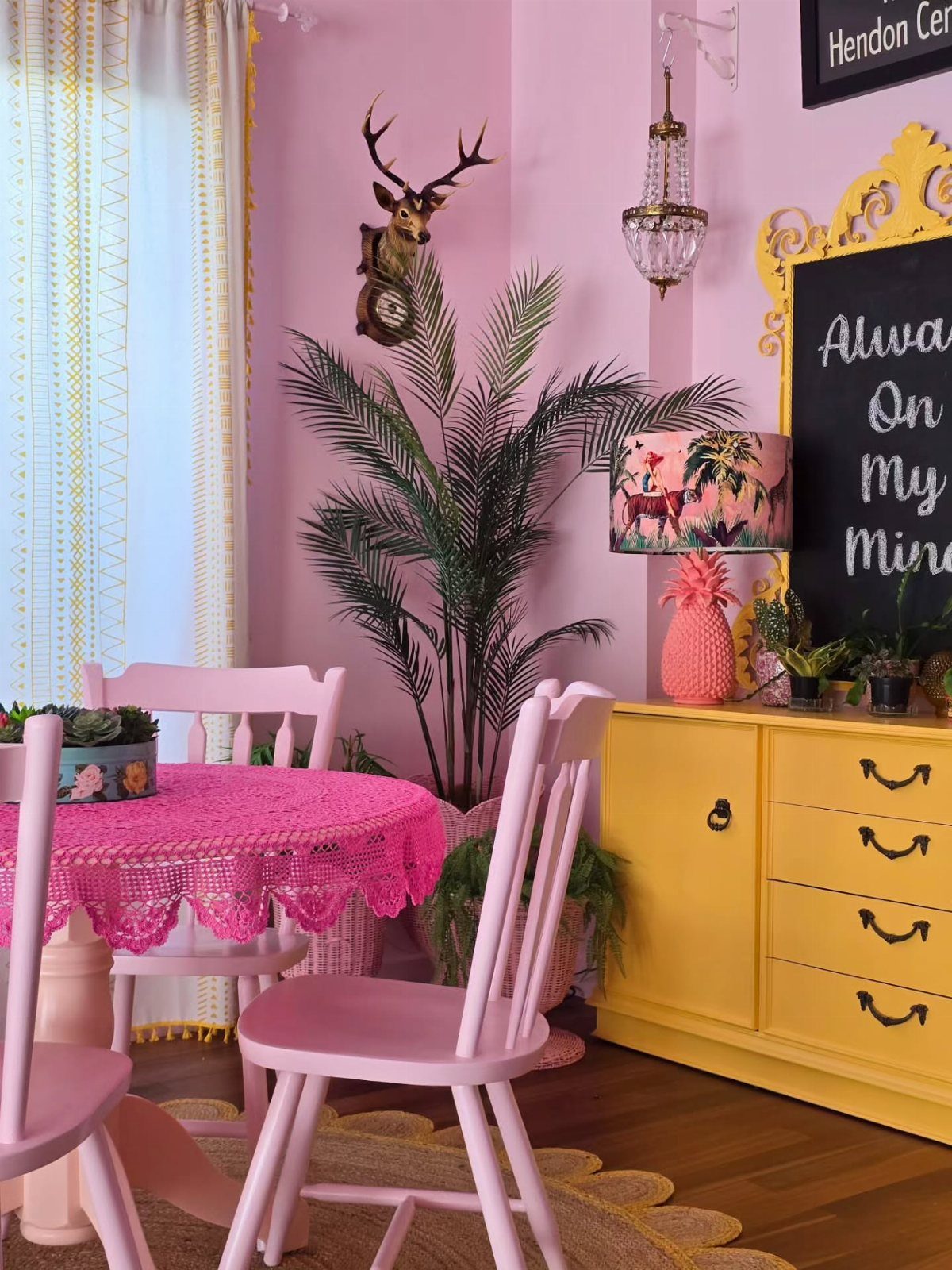 Pink dining room with yellow sideboard, pink chairs, and a deer head trophy on the wall.