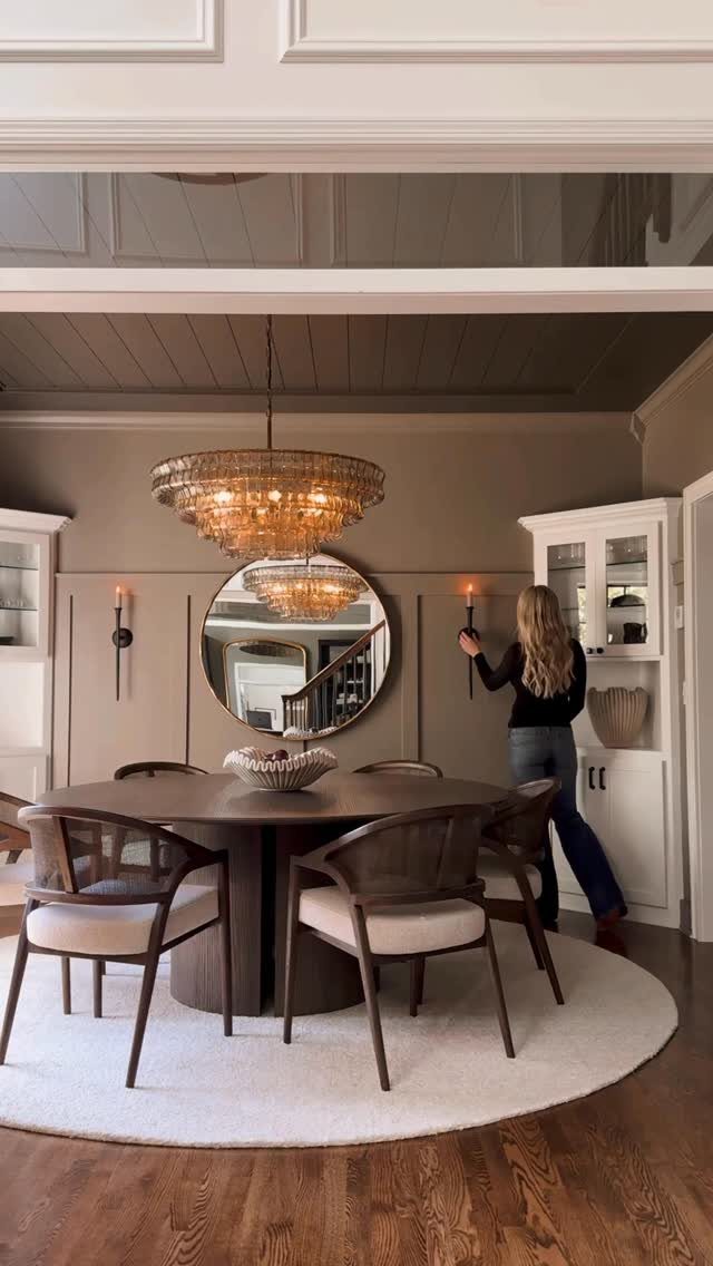 A woman reaches to touch a lit wall sconce in a decorated dining room.