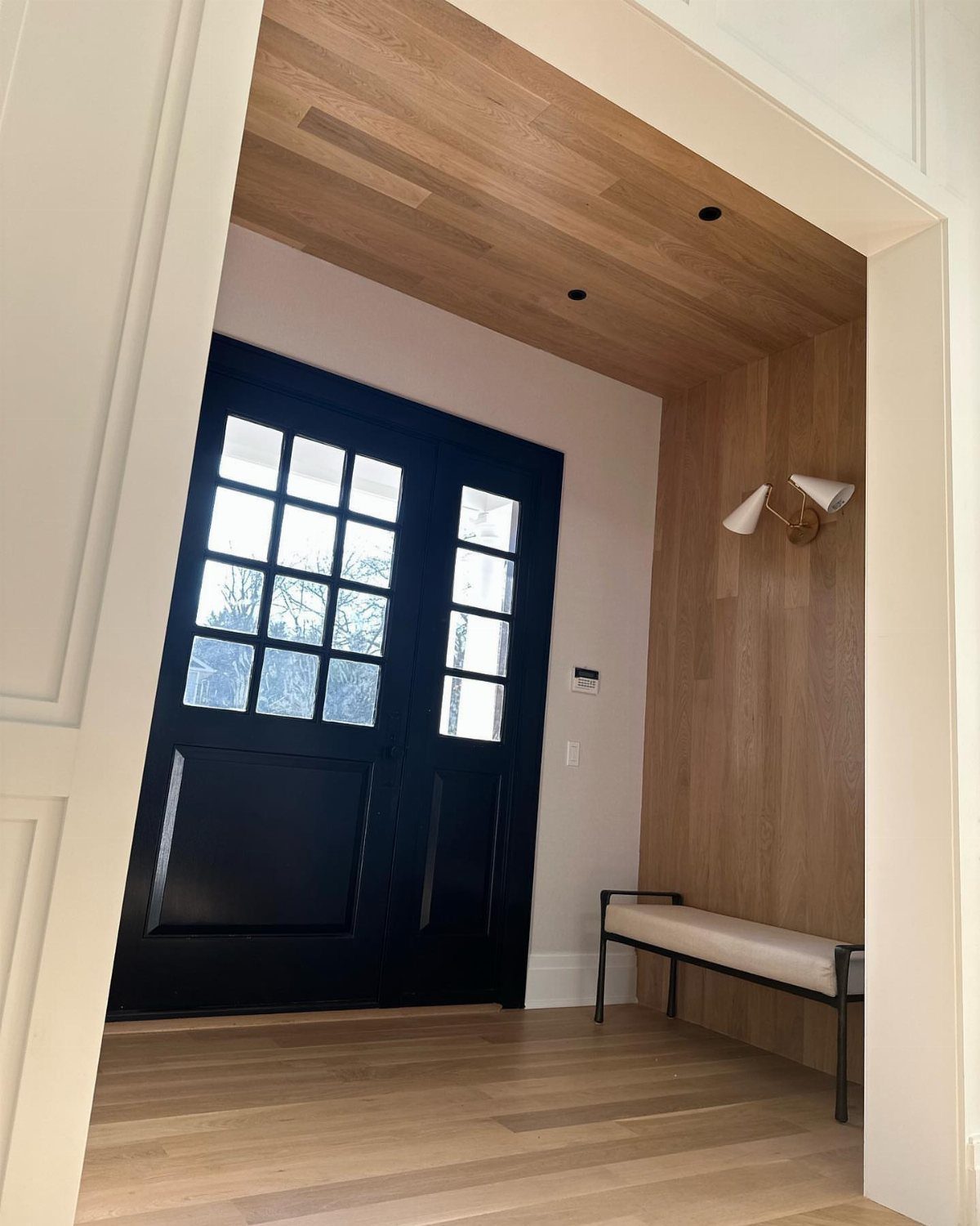 Floor to Ceiling Wall Paneling: 9 Rooms That Get It Right 7 Light wood paneling covers the walls and ceiling in a modern entryway with black doors.