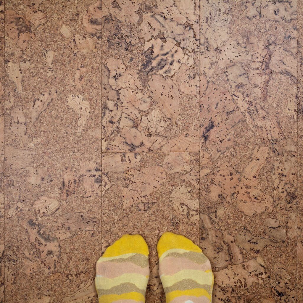 Person wearing yellow patterned socks standing on a textured cork plank floor.