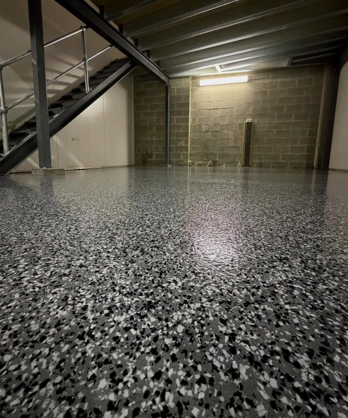 Speckled grey and black epoxy flooring in a room with concrete walls and metal stairs.