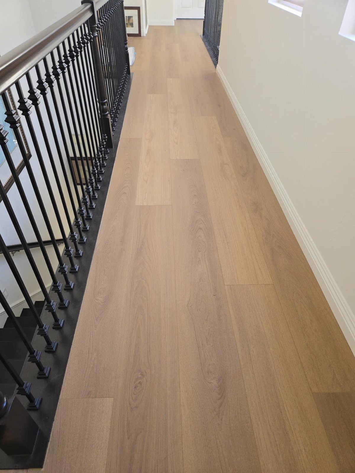 Light brown wood-look laminate flooring installed in a narrow hallway next to a black railing.