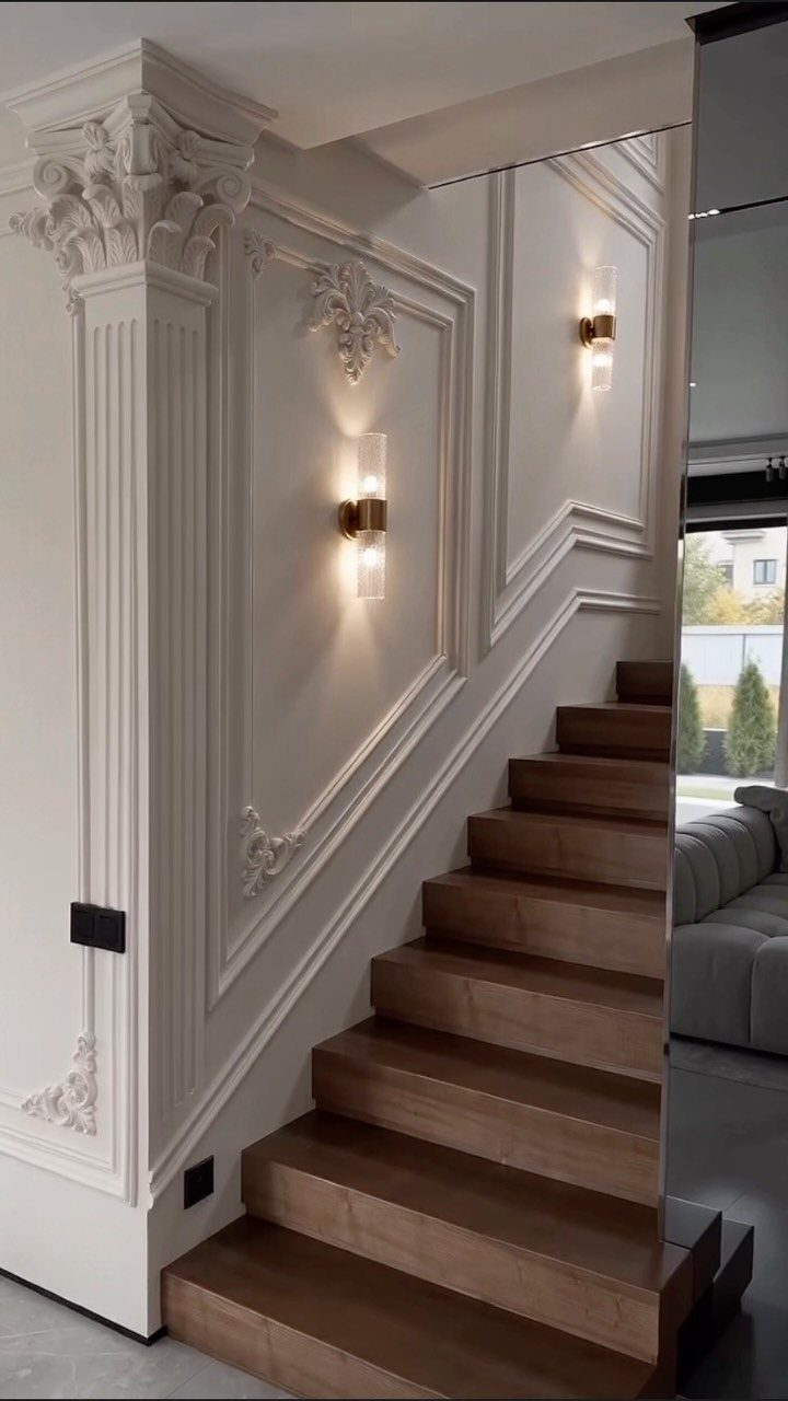 Ornate white wall molding and decorative pilasters on a wall beside a wooden staircase.