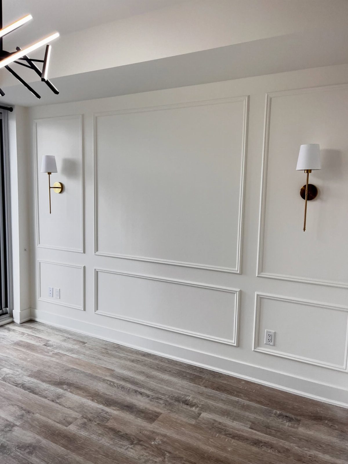 White walls decorated with rectangular french wall molding and gold wall sconces above wood floors.