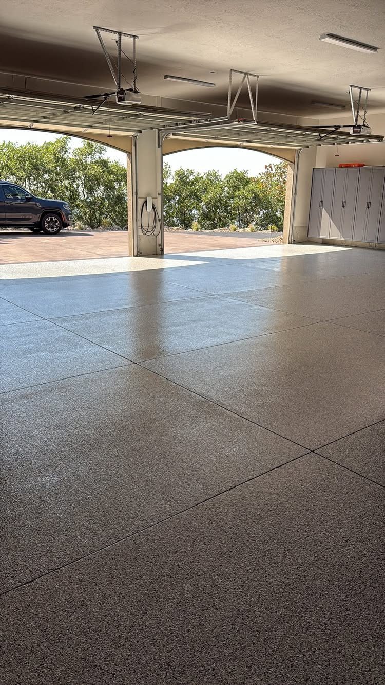 A glossy, grey speckled epoxy coating on a spacious garage floor with open garage doors.