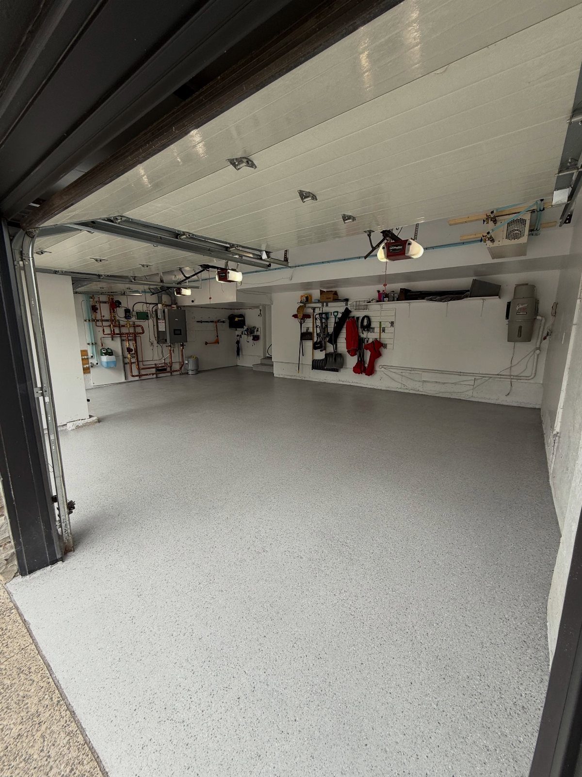 A clean garage with a light grey speckled floor and white walls with tools hanging.