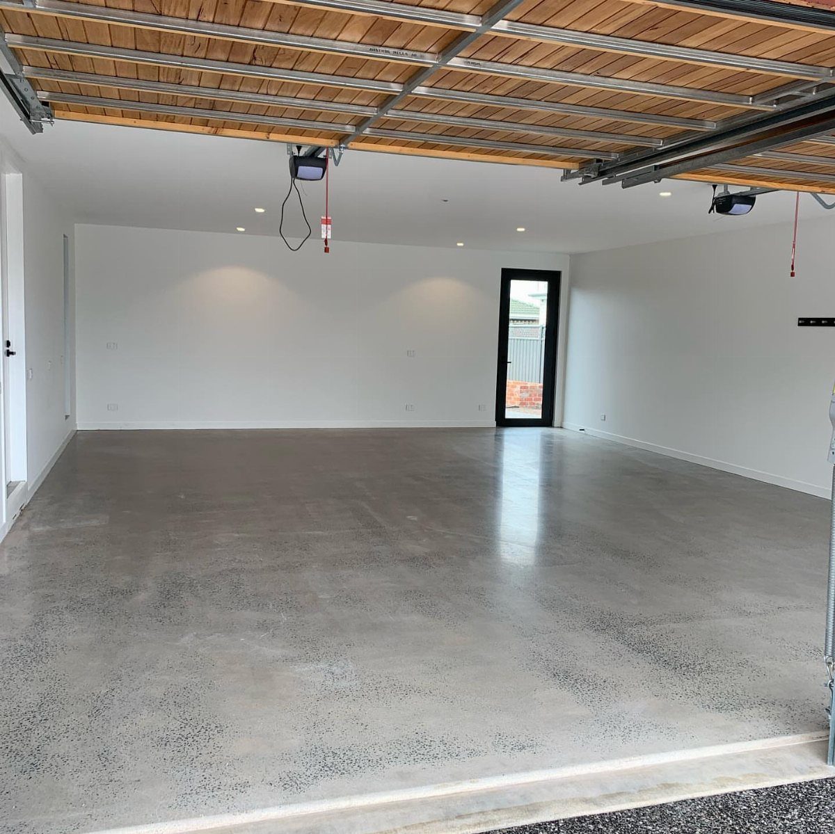 Polished concrete floor reflecting light in a large, empty white garage with wooden ceiling beams.