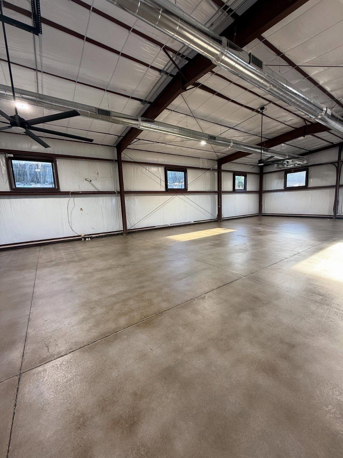 A large empty garage featuring a polished, marbled stained concrete floor and white metal walls.