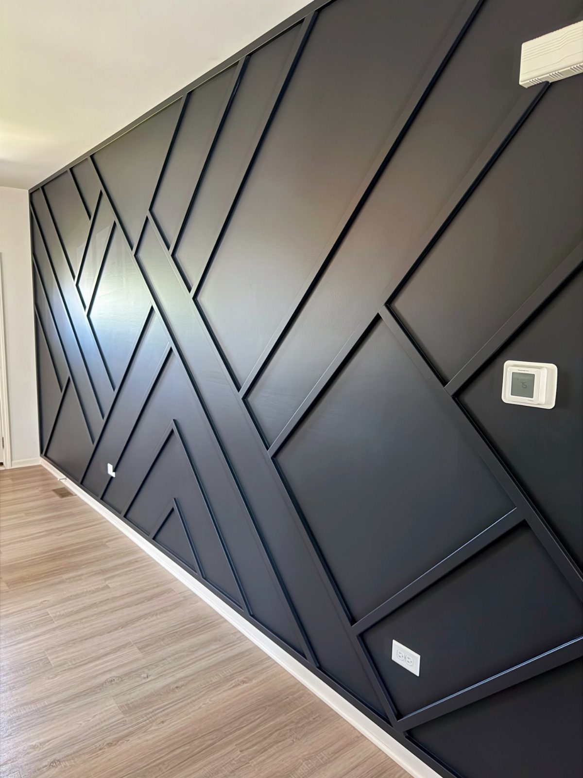 Geometric Accent Wall: 11 Ideas in Wood, Paint, and Light 6 Dark charcoal geometric accent wall with raised linear patterns and light wood flooring below.