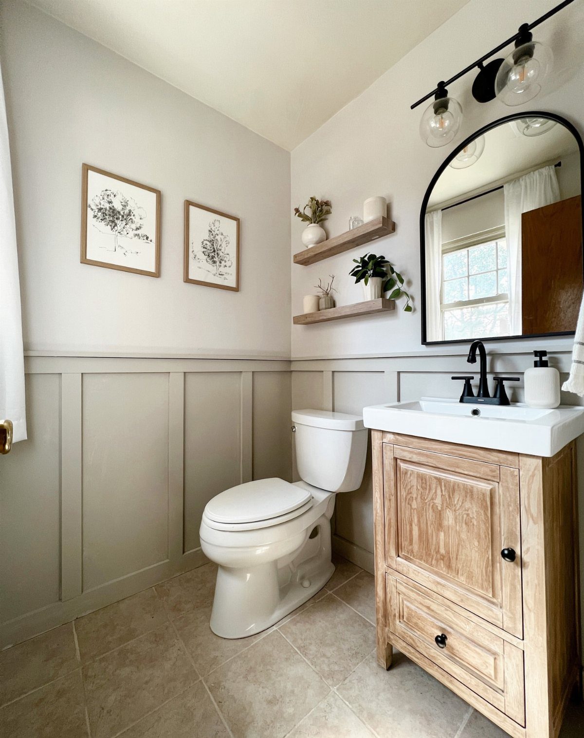 12 Half Bath Accent Wall Ideas That Work in Tight Spaces 4 Small bathroom with a white toilet, wooden vanity, arched mirror, and grey wainscoting on the walls.
