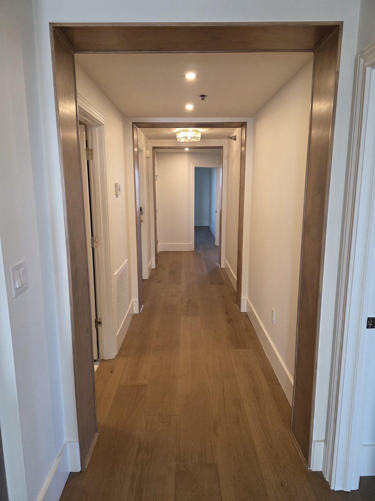 10 Hardwood Flooring Ideas for Every Room Style 10 Light-colored wood plank flooring running through a long, white hallway with wooden door frames.