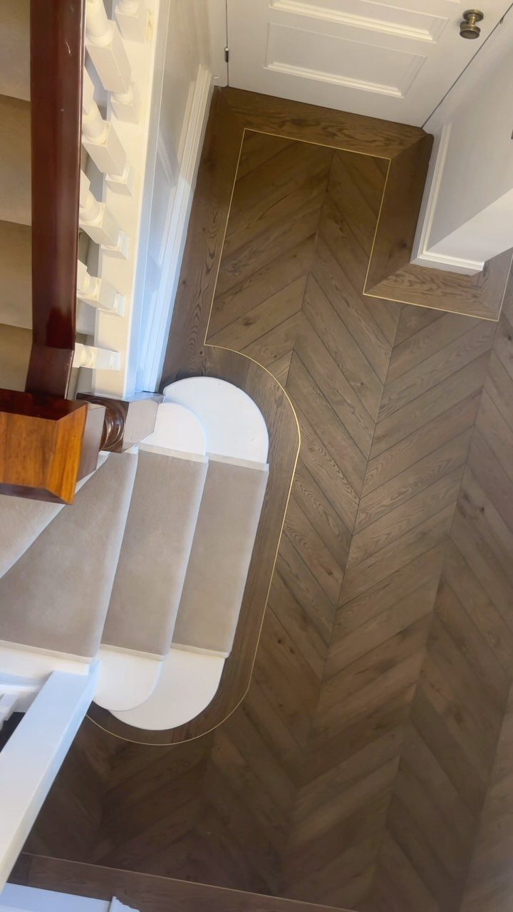 10 Hardwood Flooring Ideas for Every Room Style 6 Herringbone pattern hardwood flooring with warm brown tones and subtle gray undertones near a white staircase.