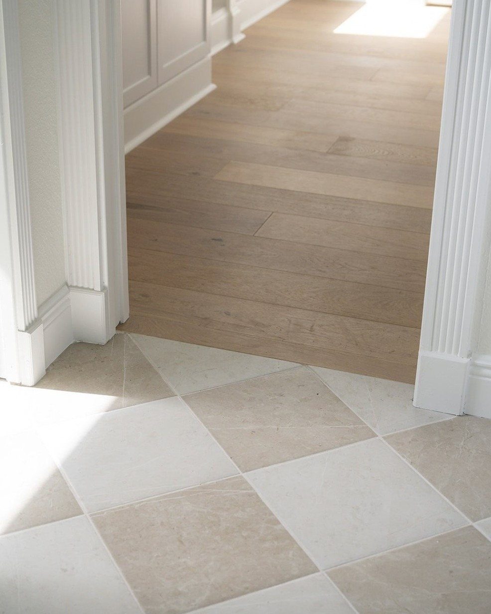 Light beige stone tiles meeting light wood plank flooring at a white doorway entrance.