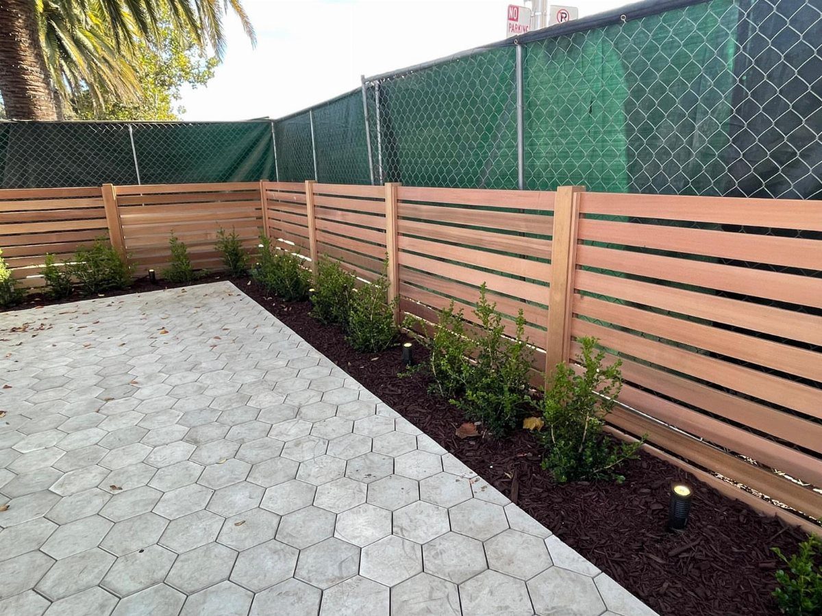 Horizontal Slat Fence: 8 Designs for Modern Backyards 8 Natural wood horizontal slat fence bordering a hexagonal tile patio with small green plants.