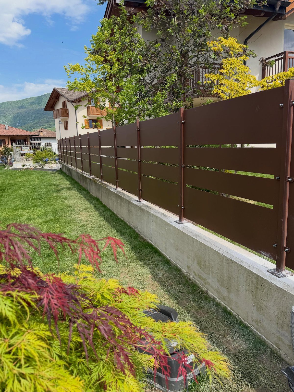 Horizontal Slat Fence: 8 Designs for Modern Backyards 3 Brown horizontal slat fence mounted on a concrete wall in a green garden setting.