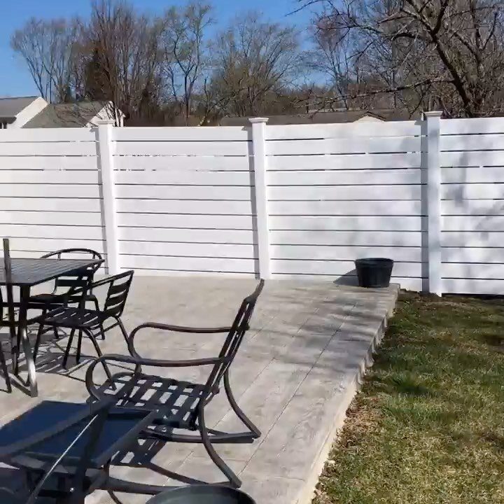 Horizontal Slat Fence: 8 Designs for Modern Backyards 4 White horizontal slat vinyl fence surrounding a stone patio with black metal outdoor furniture.