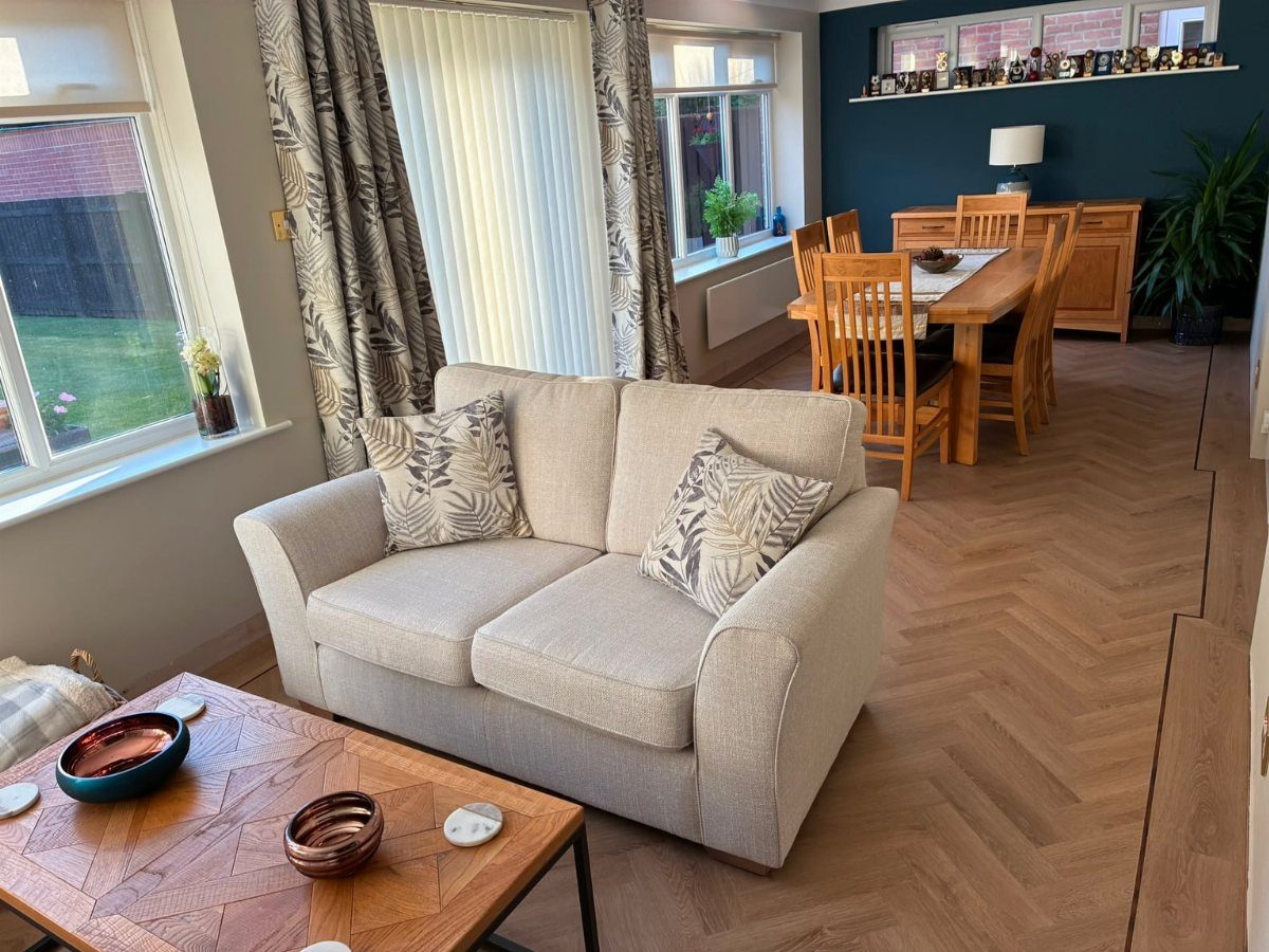 Light oak herringbone flooring in a living and dining room with a beige loveseat.