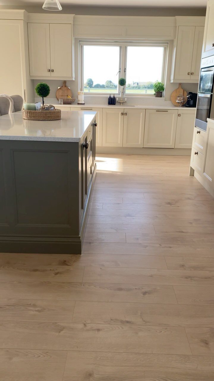 Light oak wood flooring in a bright, modern kitchen with white cabinetry and a grey island.