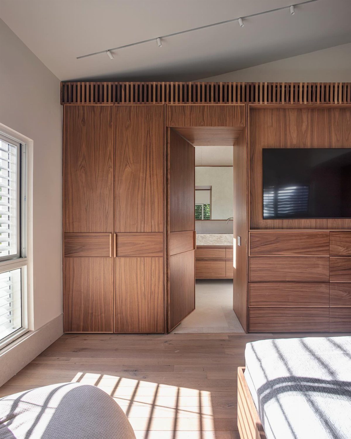 Light wooden floor in a modern bedroom with walnut wood built-in wardrobes and sunlight.