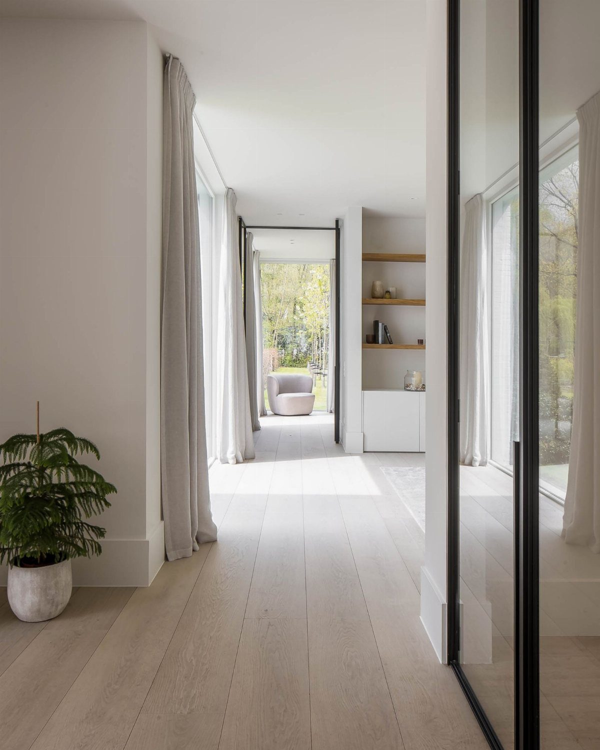 Light wooden plank flooring in a bright, modern hallway with white walls and flowing curtains.