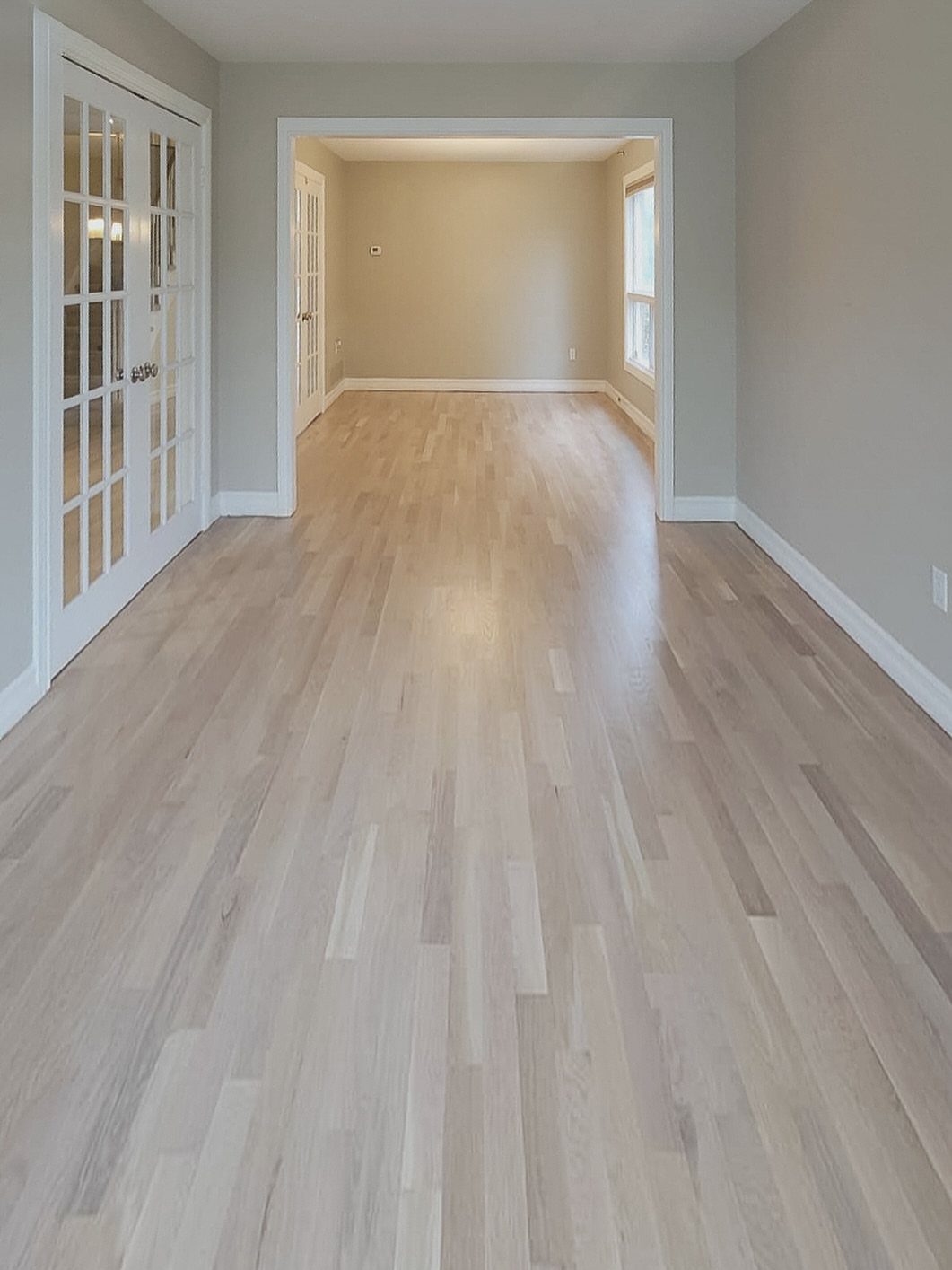 Light wooden plank flooring extending through an open doorway into an empty room with grey walls.