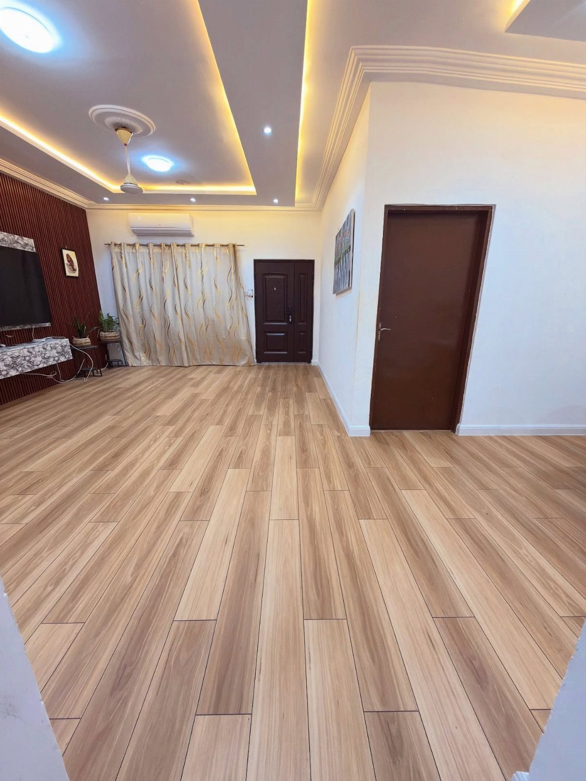 Light brown wood-look tile flooring installed in a spacious room with white walls and a brown door.