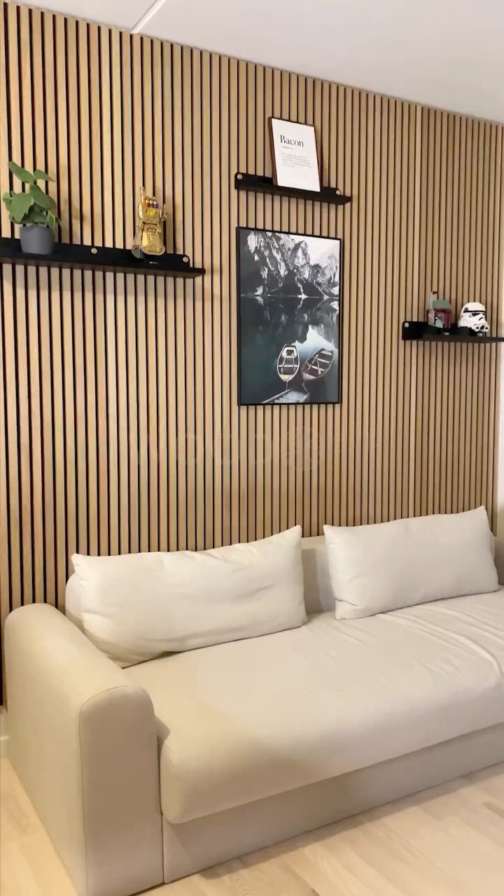 Vertical light wood slat panels on a wall behind a white sofa with black shelves.