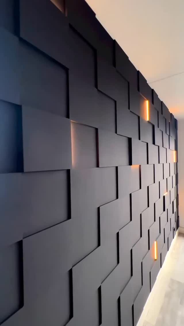 Dark geometric wall panels with warm orange light glowing from the recessed gaps between them.