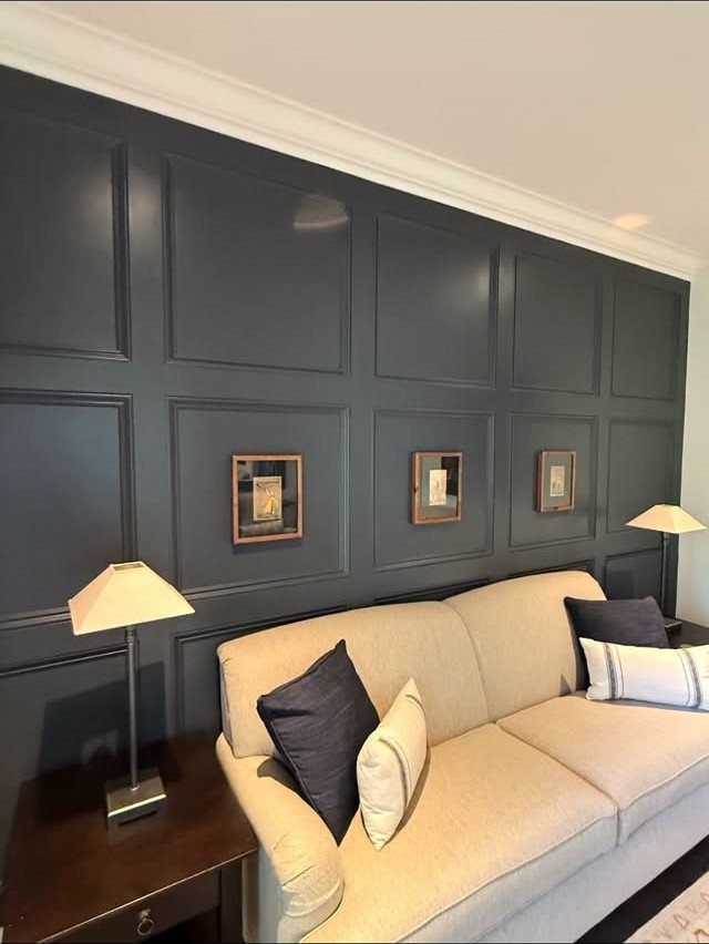 Dark blue paneled wall with rectangular moulding behind a cream sofa and small framed pictures.