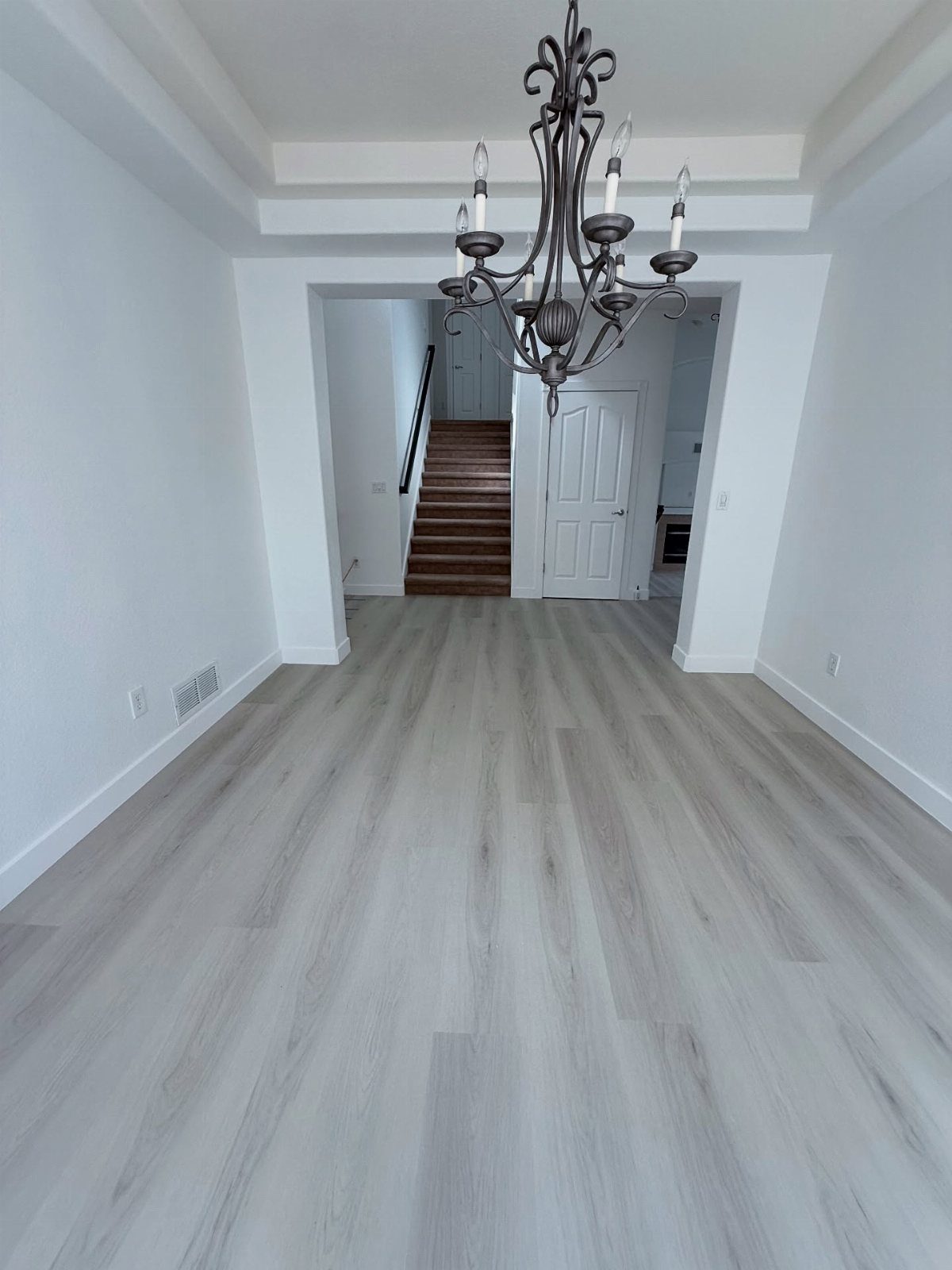 Light gray wood-look flooring in an empty room with white walls and a chandelier.
