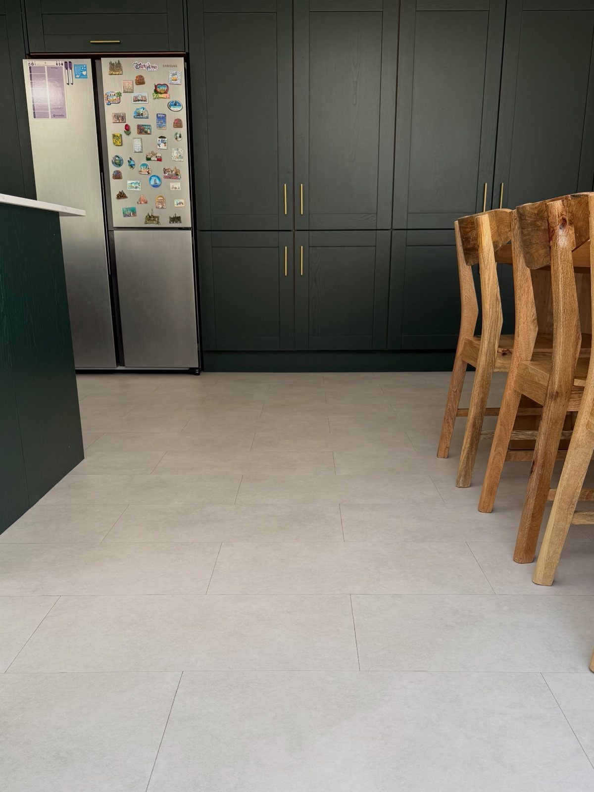 Cream colored floor tiles in a kitchen with dark green cabinets and wooden chairs.